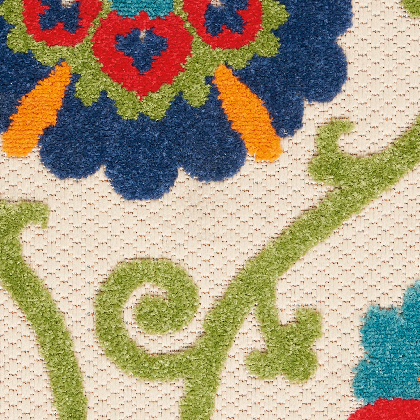 Close-up of a tufted floral rug: cobalt blue petals, red centers, orange accents, lime-green vine swirls on beige background.