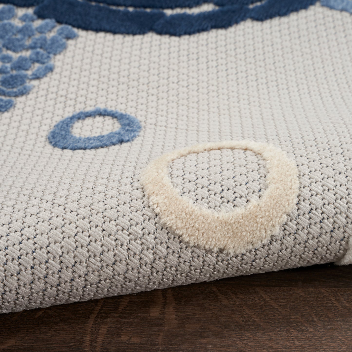 Light gray woven runner rug with blue circular motifs and a beige loop tuft on dark wood floor.