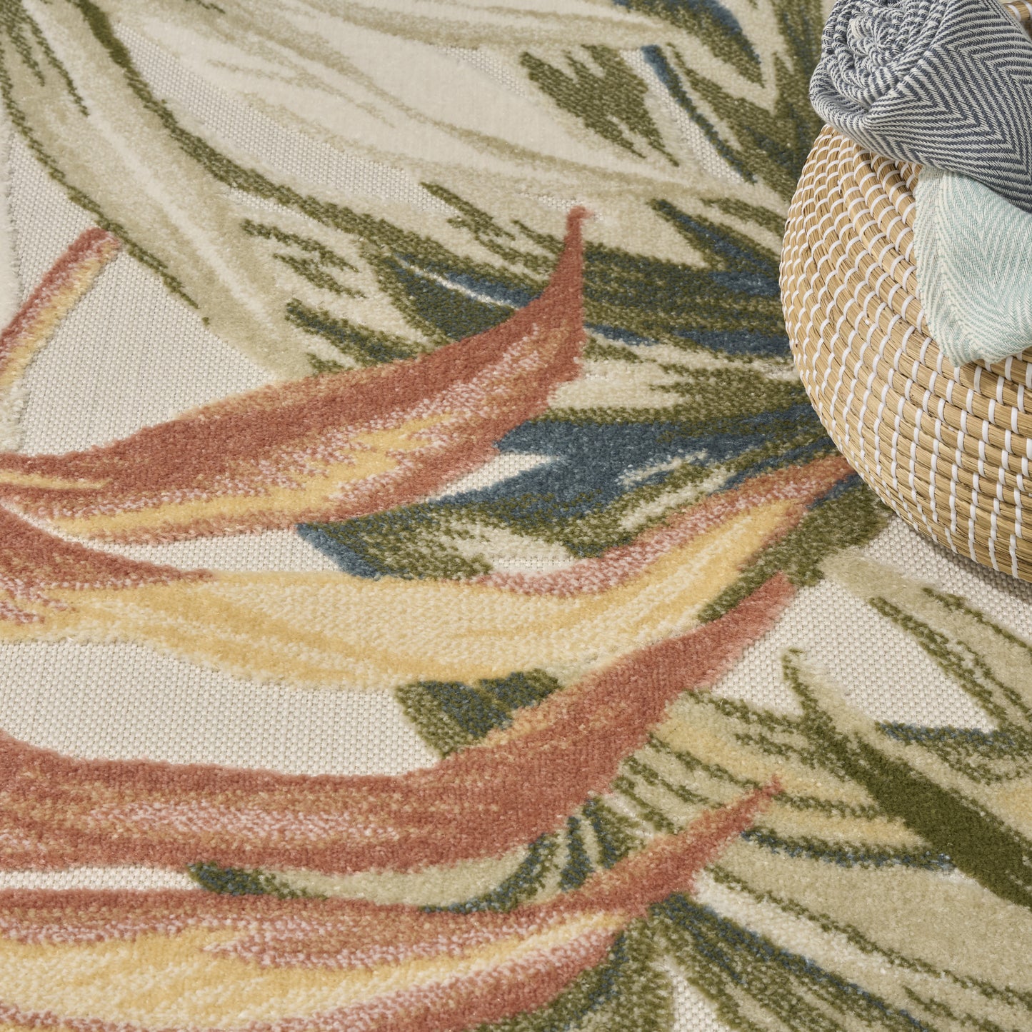 Close-up of a textured cream rug with leaf-like pattern in green, yellow, rust beside a woven rattan basket with striped fabrics.