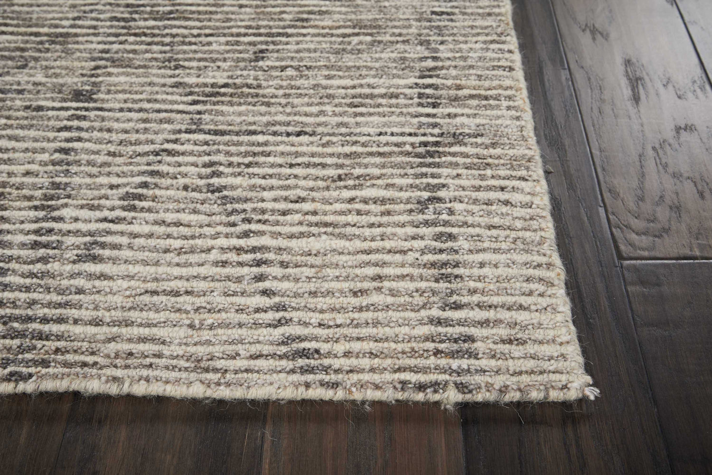Beige textured area rug with brown horizontal stripes and fringed edge on dark wooden floor.
