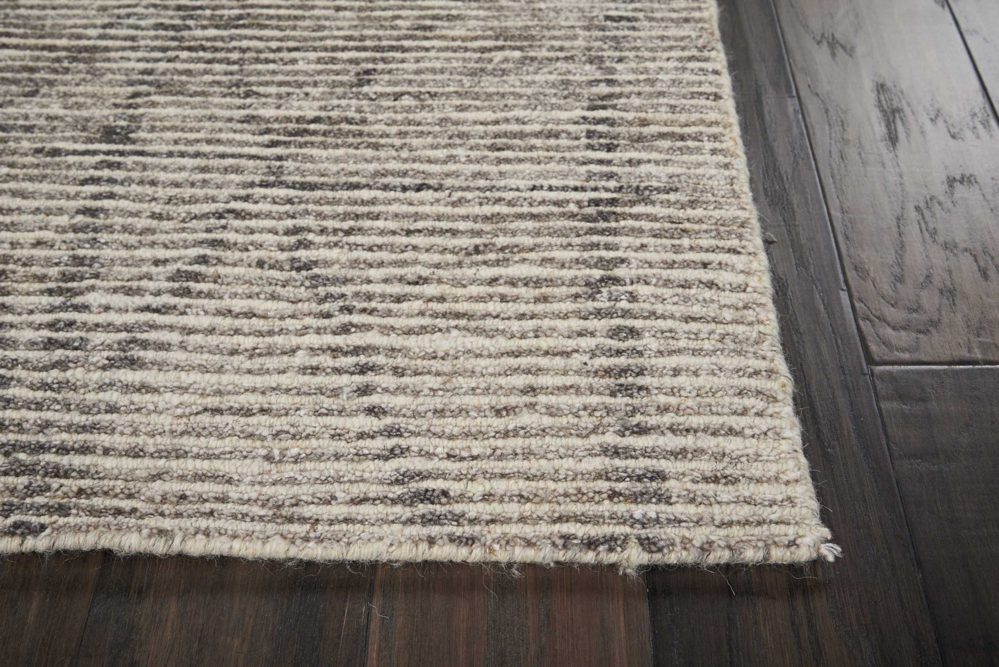 Beige textured area rug with brown horizontal stripes and fringed edge on dark wooden floor.