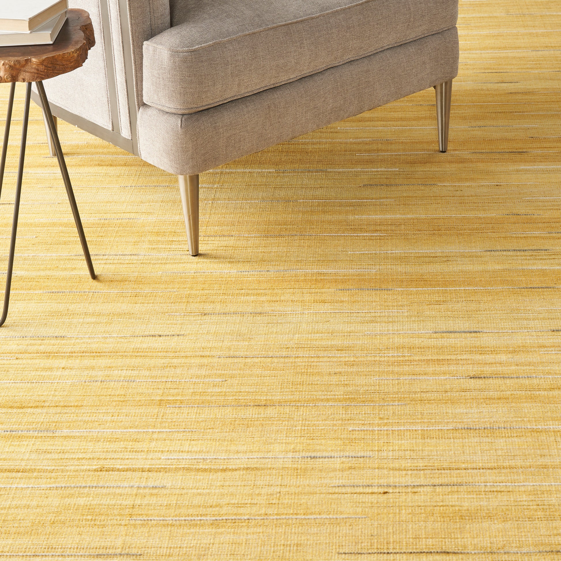 Golden-yellow striped rug with beige tones; a beige upholstered sofa and a round live-edge wood side table nearby.