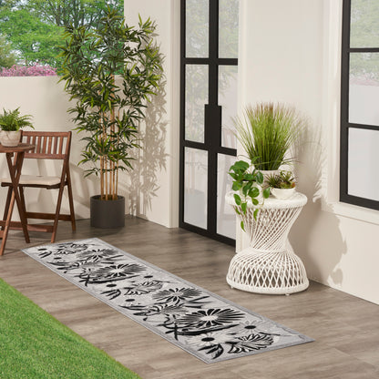 Gray floral runner rug on wood floor beside wicker table, potted plants, and black-framed glass doors.