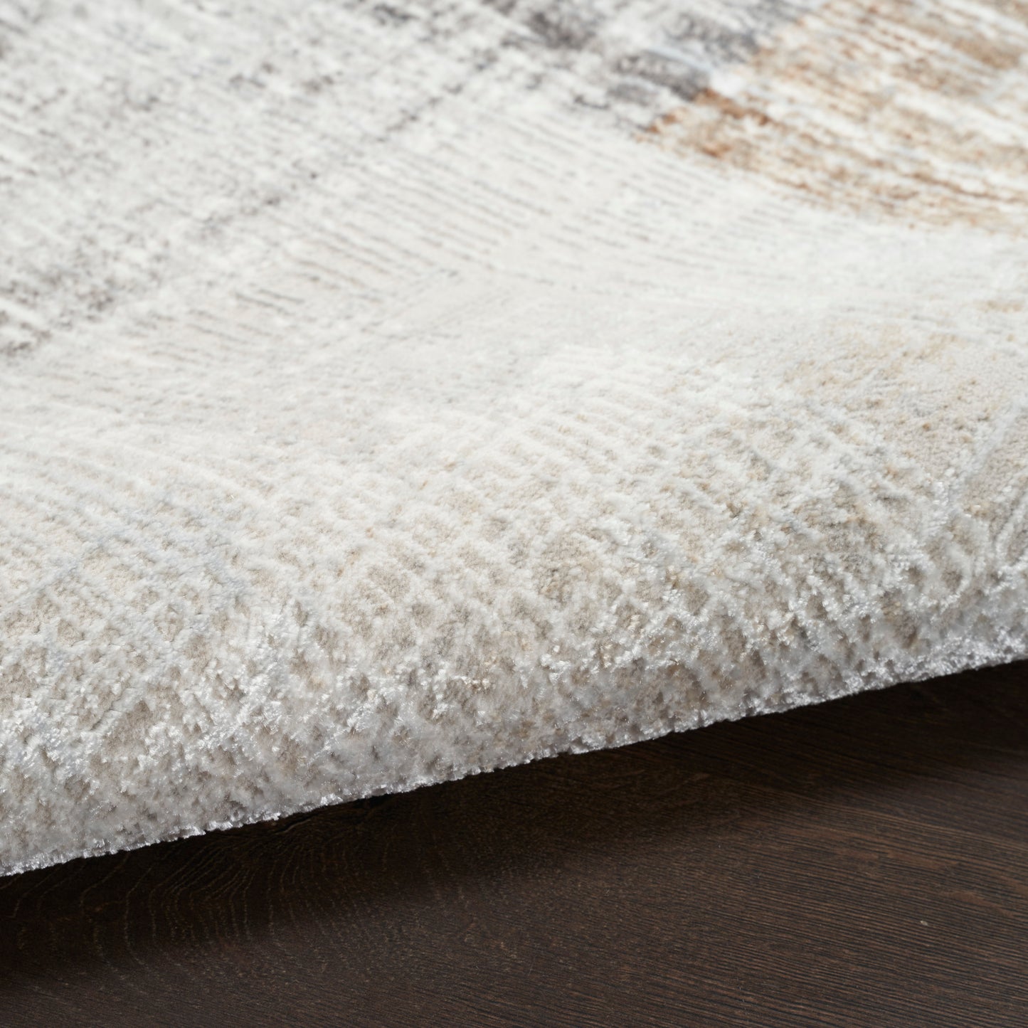 Close-up of a plush cream-beige area rug with a subtle textured pattern on dark wood floor.