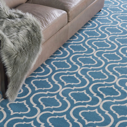 Blue and white trellis-pattern rug beside a tan leather sofa with a grey faux-fur throw draped over the arm.