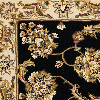 Oriental rug with a black central field and cream border, featuring gold, ivory, and burgundy floral motifs.
