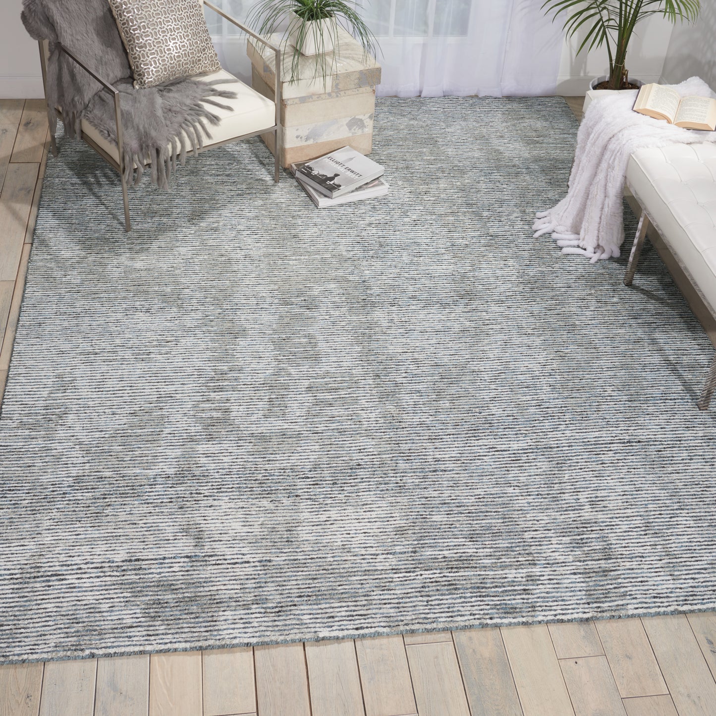Blue-gray woven area rug in a cozy living room with wooden floor, pallet coffee table, chair, plants, books, and a white daybed.