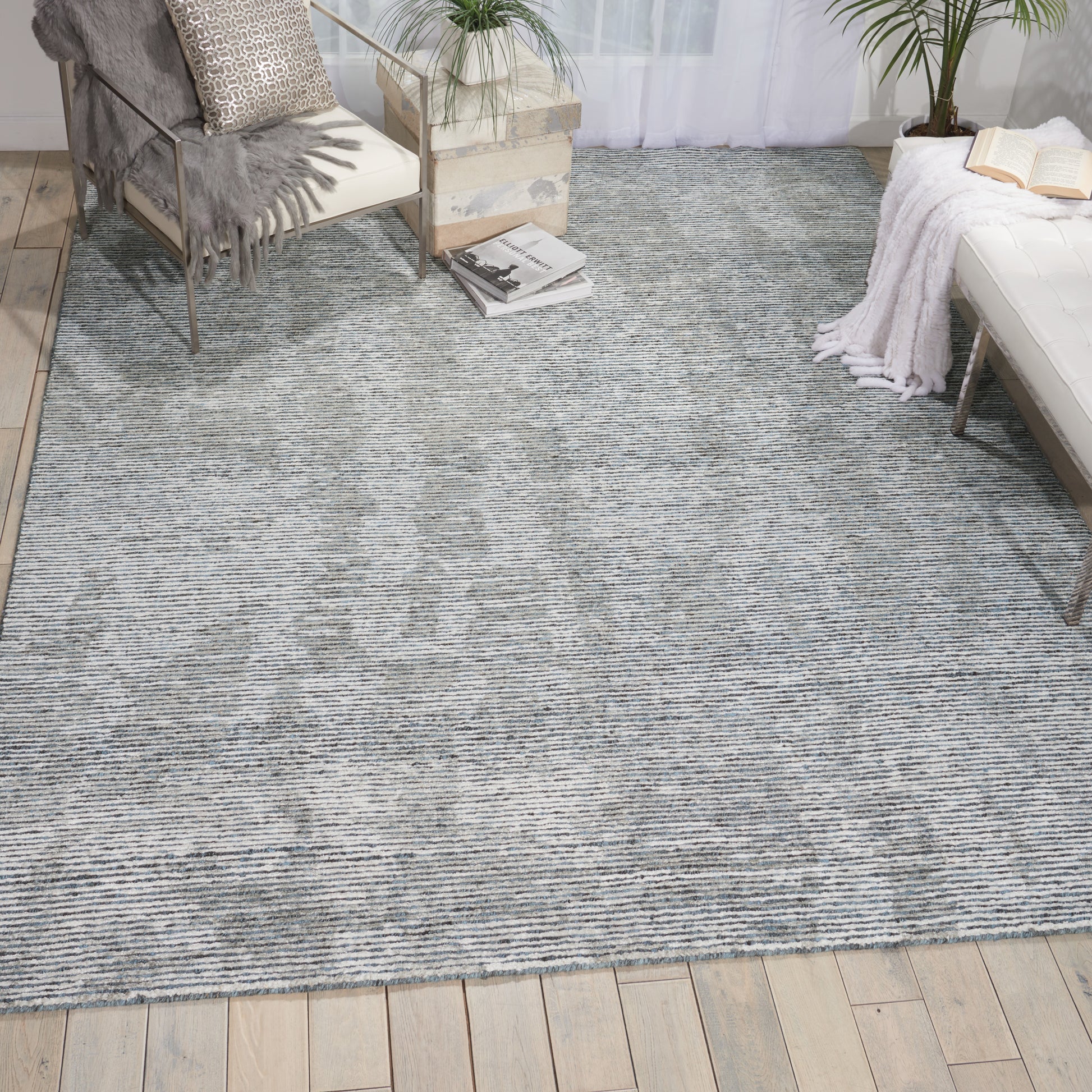 Blue-gray woven area rug in a cozy living room with wooden floor, pallet coffee table, chair, plants, books, and a white daybed.