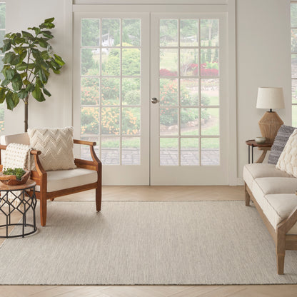Neutral living room with a light beige woven area rug, wooden-framed chairs, cream sofa, potted plant, and French doors.