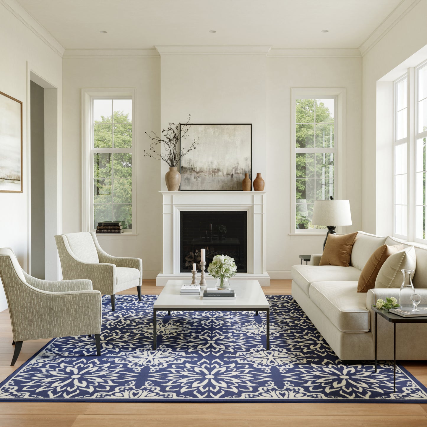 Bright neutral living room with cream sofa and armchairs, navy floral rug, white coffee table, fireplace, art.