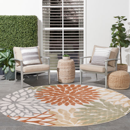 Outdoor patio seating with beige armchairs, round multicolor outdoor rug in orange, beige, and gray, wicker side tables, and green plants.