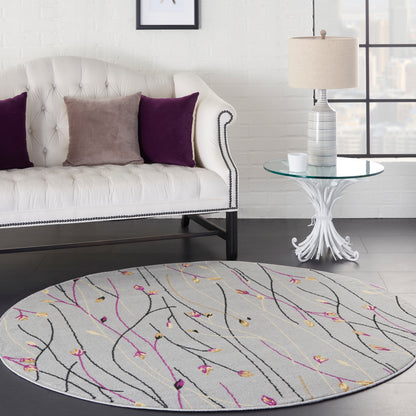 Round gray rug with black, pink and gold abstract lines; white tufted sofa with purple and taupe cushions; glass table.