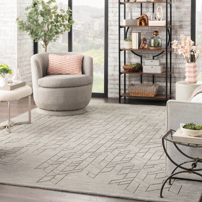 Light gray geometric rug in a sunlit modern living room, with a pink-cushioned chair and a dark metal bookshelf.