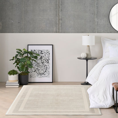 Modern minimalist bedroom with white bedding, beige rug, potted plant, framed art, black round side table and white lamp.