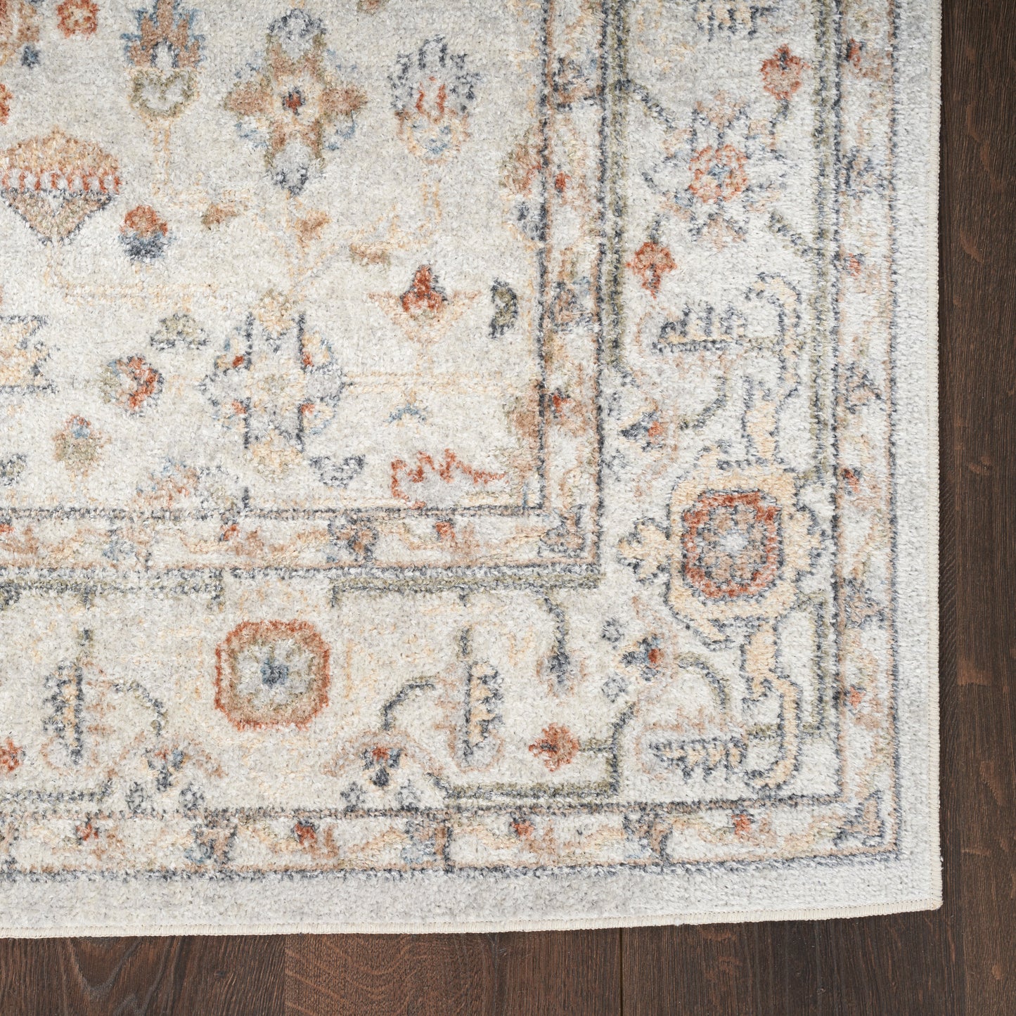 Ivory oriental rug with blue, rust and gray floral motifs and a decorative border, distressed plush pile on dark wood floor.