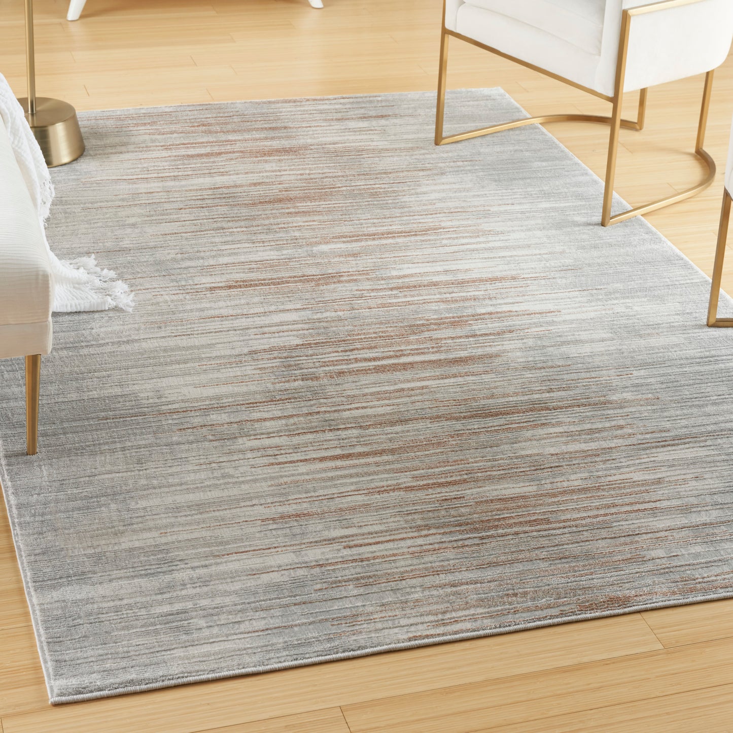 Soft grey rug with subtle rust-orange streaks on light wood floor, modern living room with white furniture and gold legs.