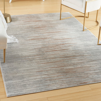 Soft grey rug with subtle rust-orange streaks on light wood floor, modern living room with white furniture and gold legs.