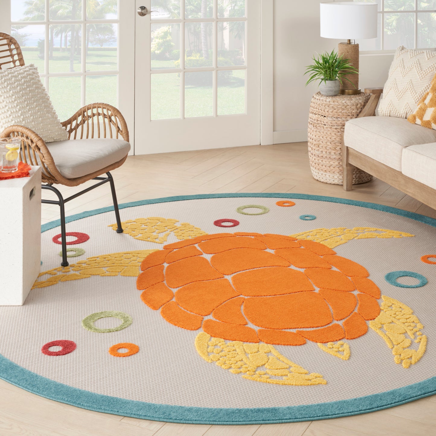 Round coastal rug with bright orange turtle design, yellow fins, teal border, and ring accents in a living room.