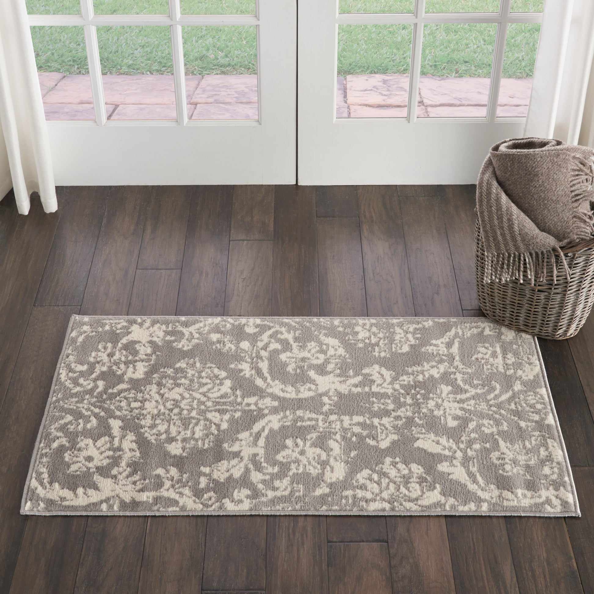 Rectangular gray and ivory damask area rug on dark wood floor, with a wicker basket and throw near French doors.