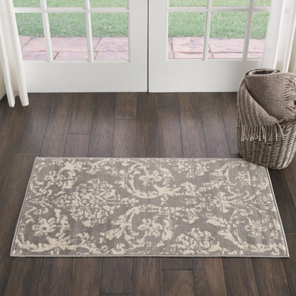 Rectangular gray and ivory damask area rug on dark wood floor, with a wicker basket and throw near French doors.