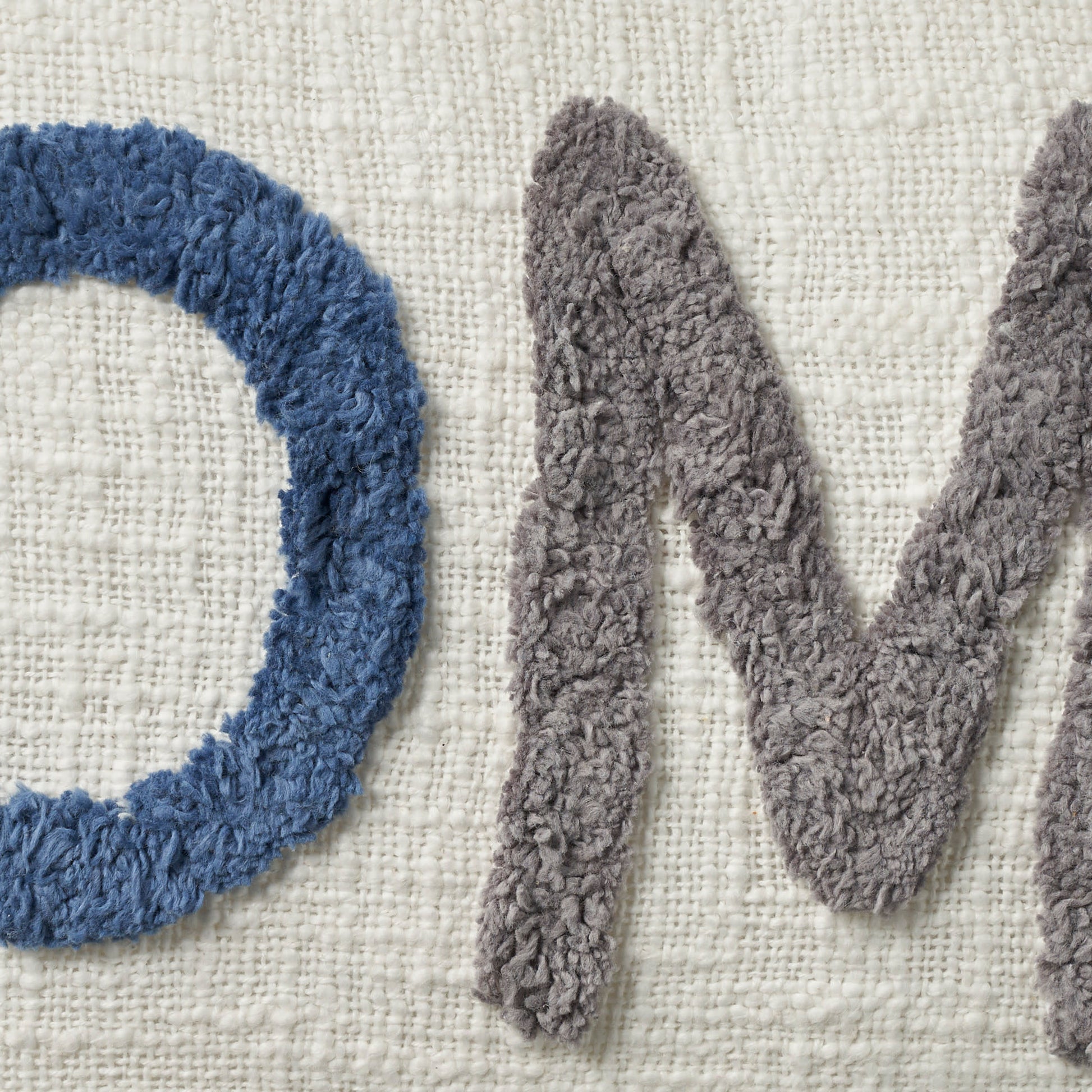 Close-up of blue shaggy O & gray plush M on a cream woven rug.