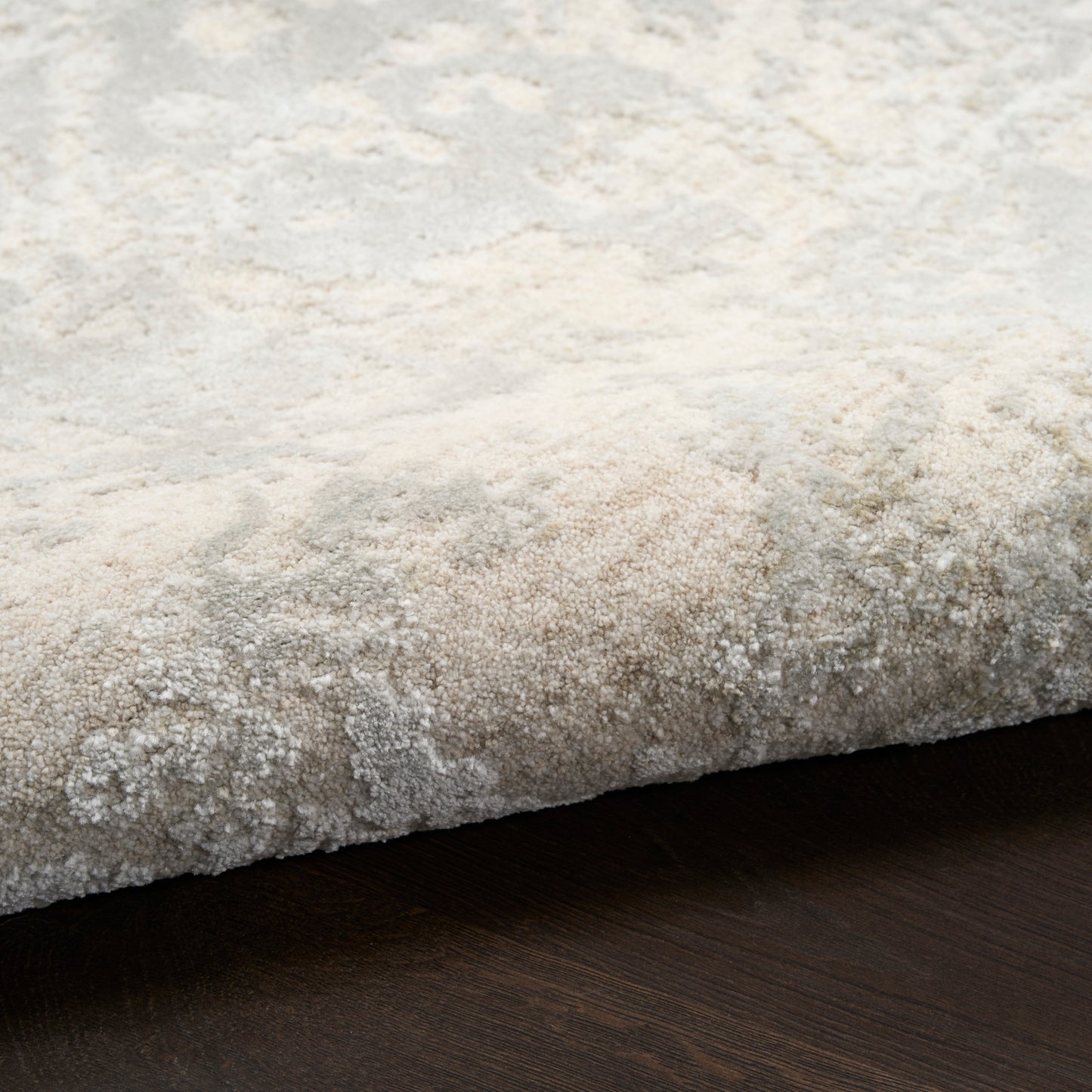 Beige plush area rug with textured pile & folded edge over dark wood floor; cozy contemporary living room style.