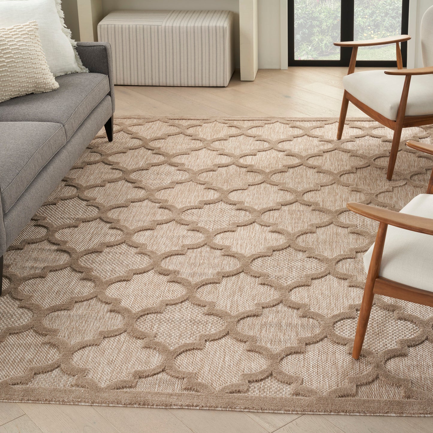 Beige woven area rug with taupe interlocking lattice trellis pattern in a modern living room with gray sofa.