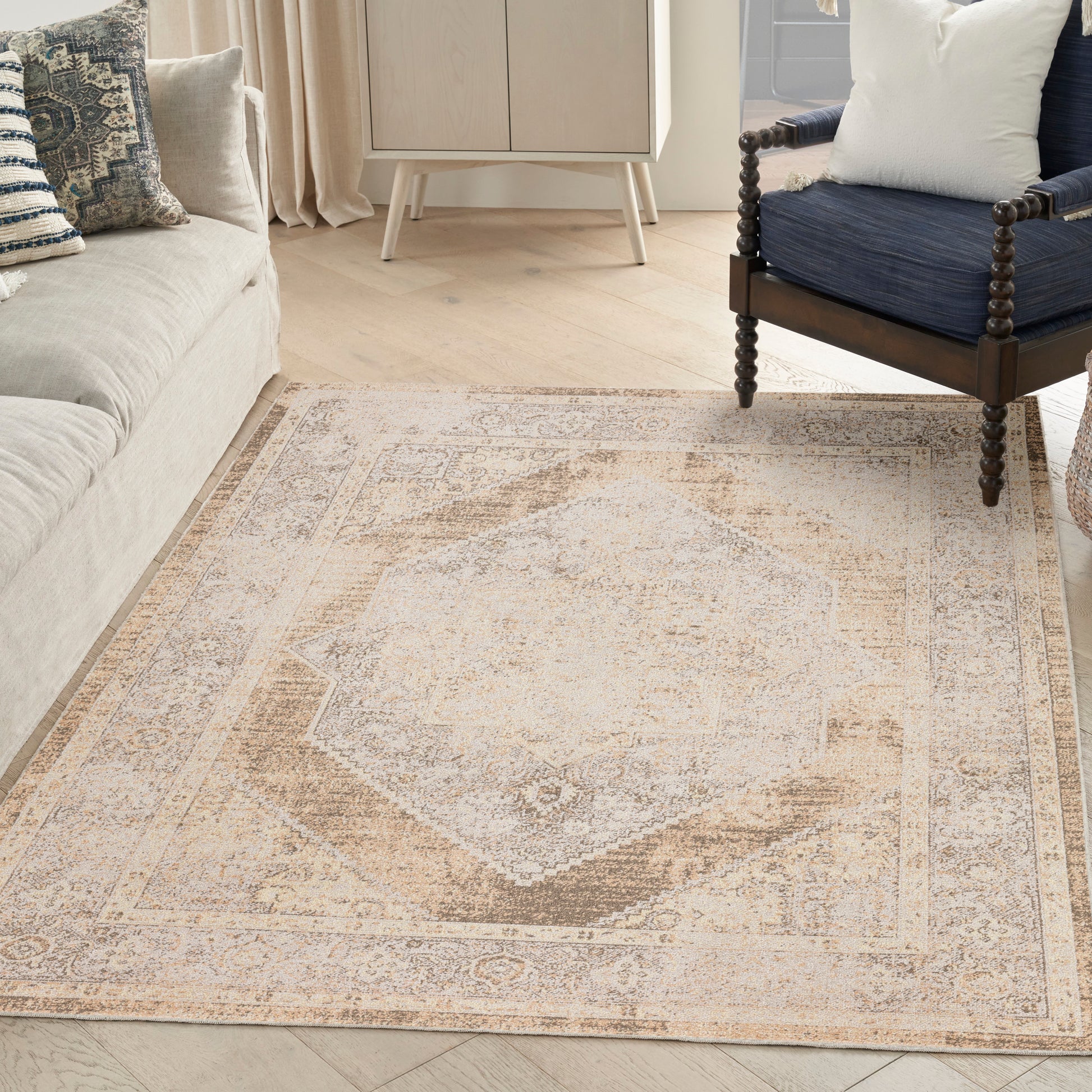 Neutral vintage-style area rug with a central beige/taupe medallion on light wood floor beside a beige sofa and navy chair.