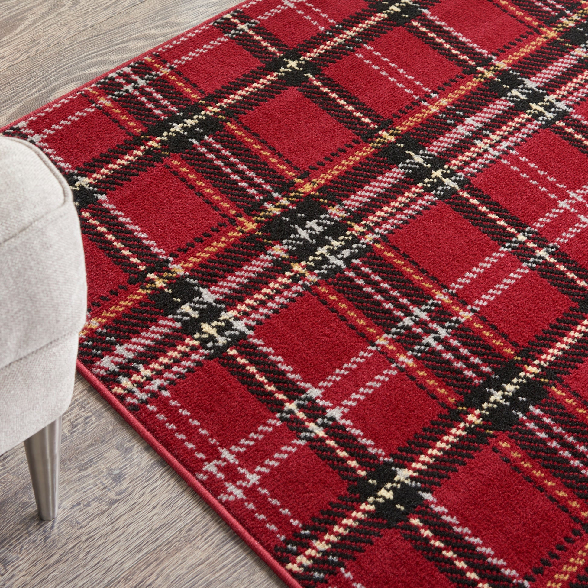 Red plaid rug with black, white, and yellow stripes on a wood floor beside a gray upholstered chair.