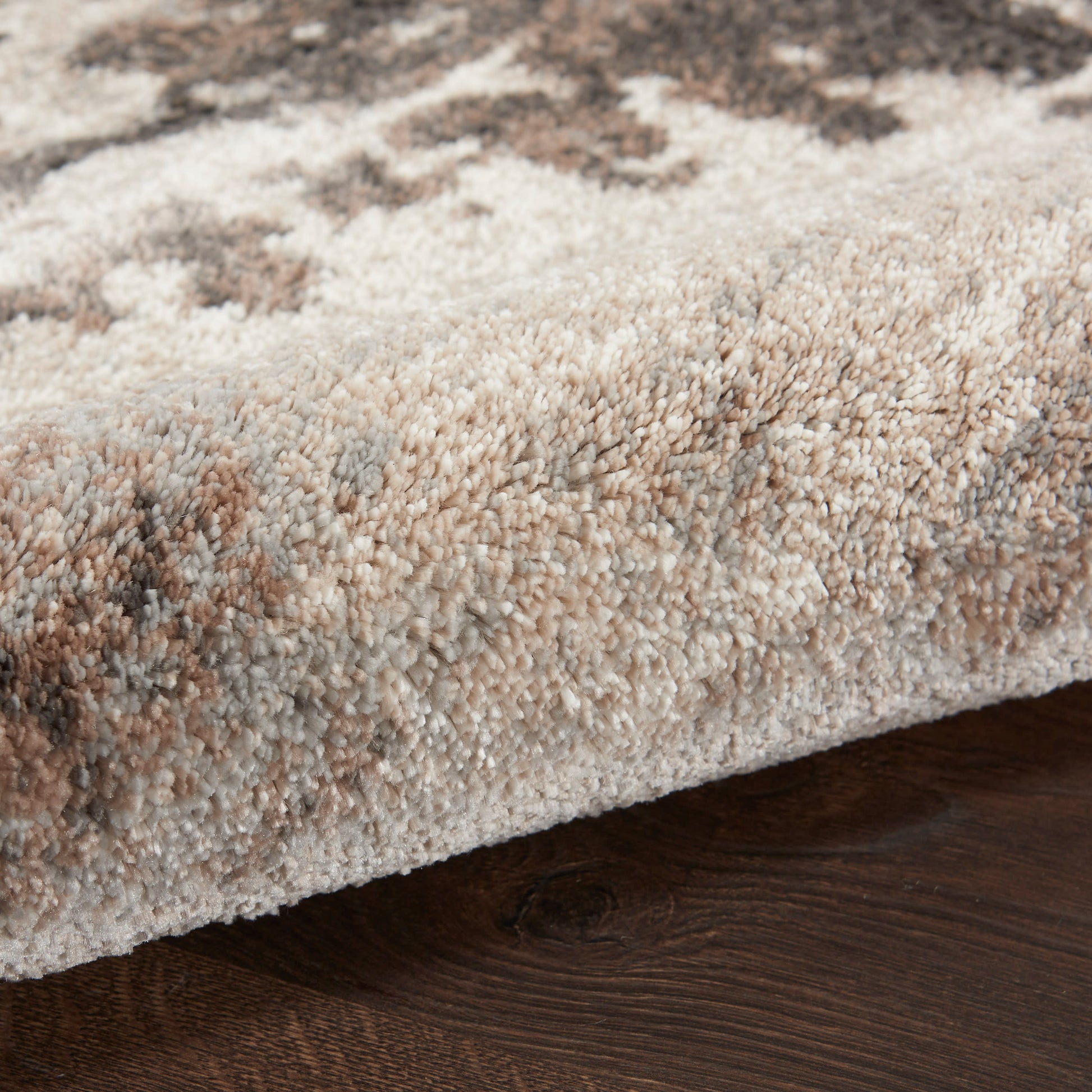 Close-up of a plush beige and taupe patterned area rug with soft pile on a dark wood floor.