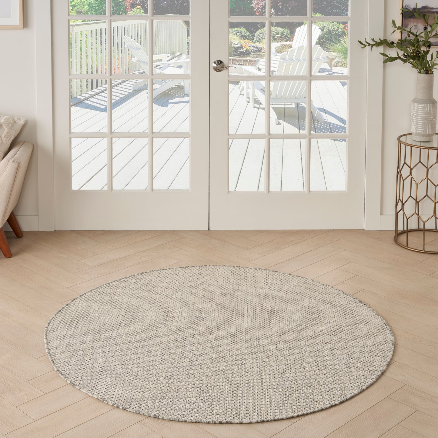 Round beige woven rug on light wood floor in front of glass French doors opening to an outdoor deck.