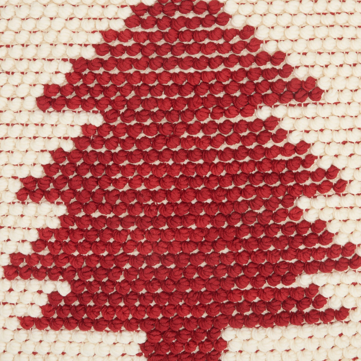 Red knitted maple-leaf motif on cream woven fabric, decorative textile.