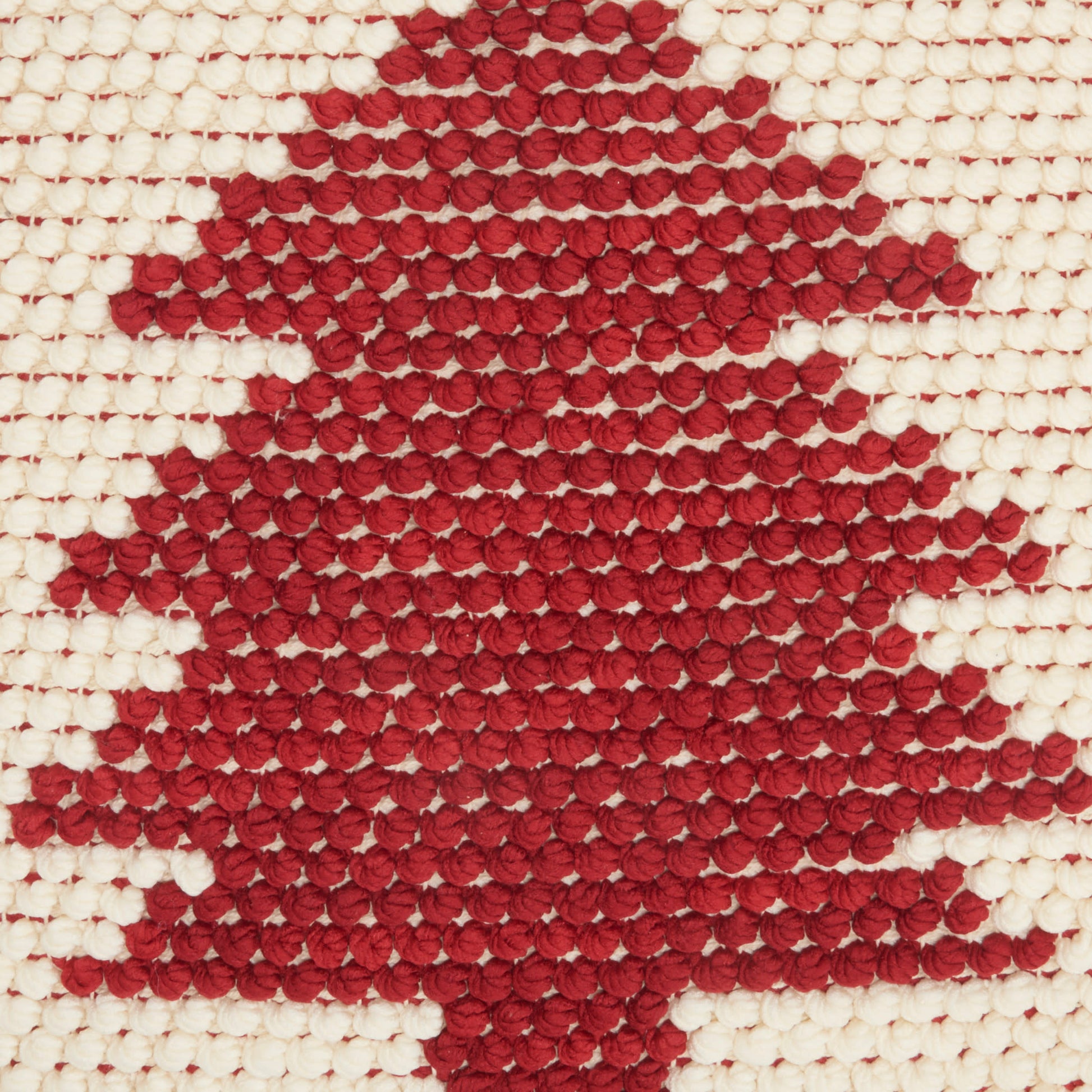 Red knitted maple-leaf motif on cream woven fabric, decorative textile.