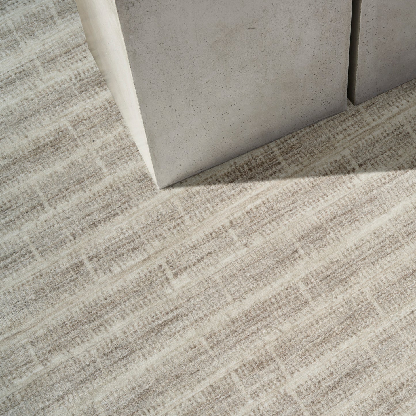 Gray concrete block corner resting on beige woven rug with a subtle rectangular grid pattern.