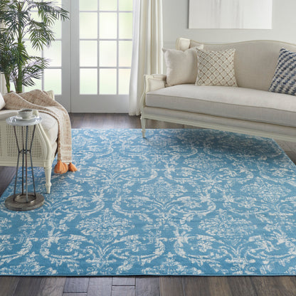 Blue damask-patterned area rug on a dark wood floor in a bright living room with a beige sofa and throw pillows