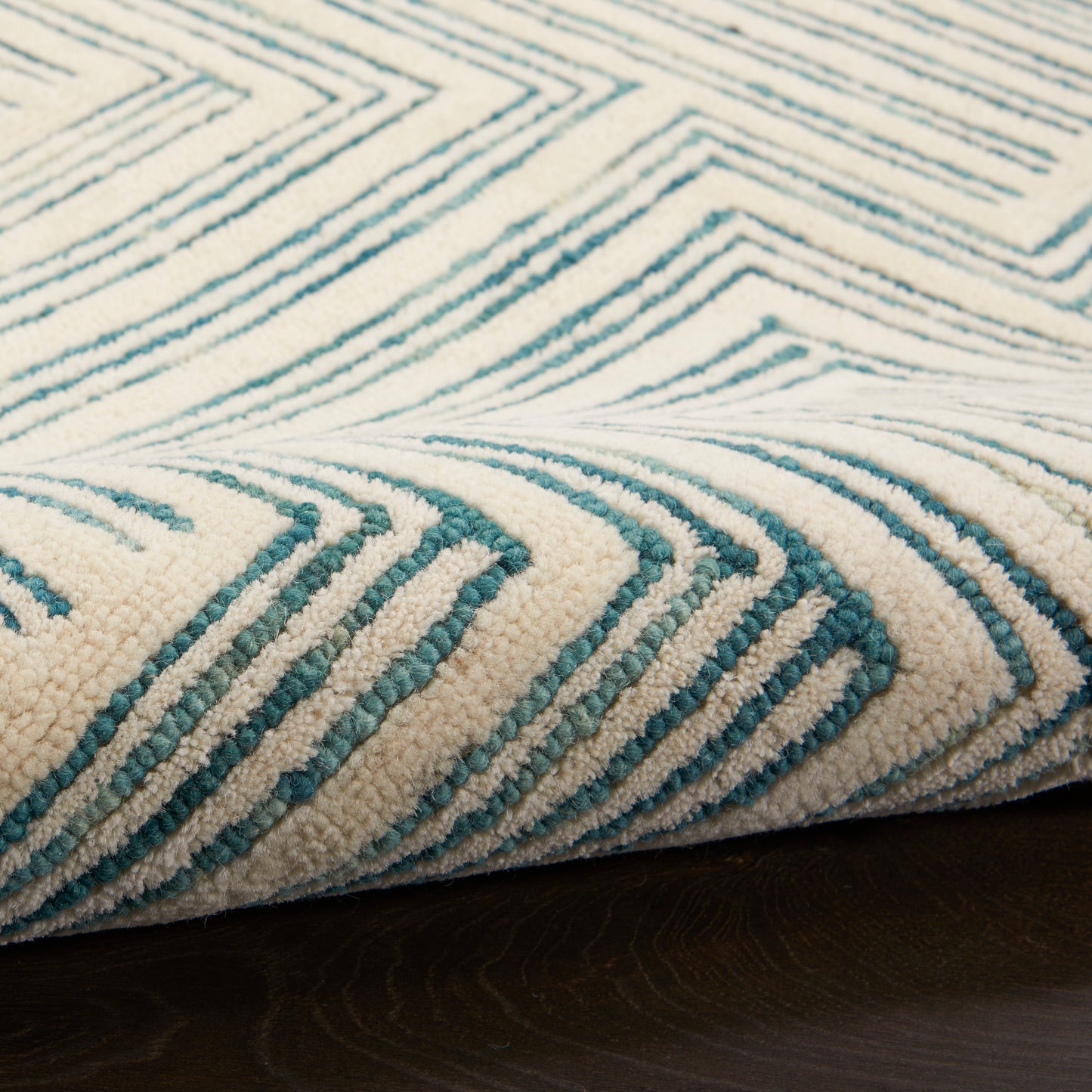 Beige base with teal geometric chevron pattern and plush shag pile on dark wood floor.