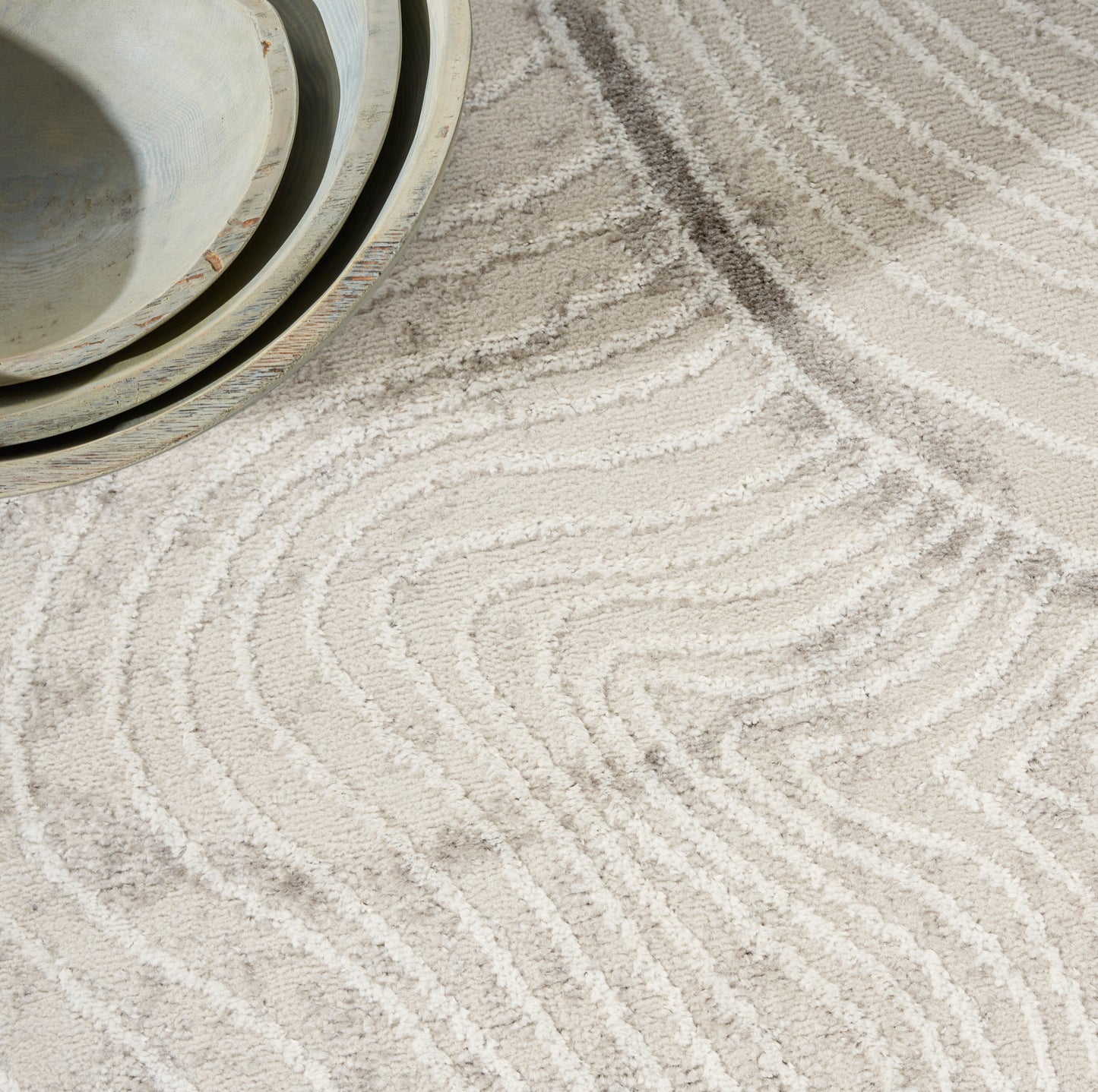 Beige tufted rug with white wavy lines; shallow ceramic bowls in pale blue-gray tones.