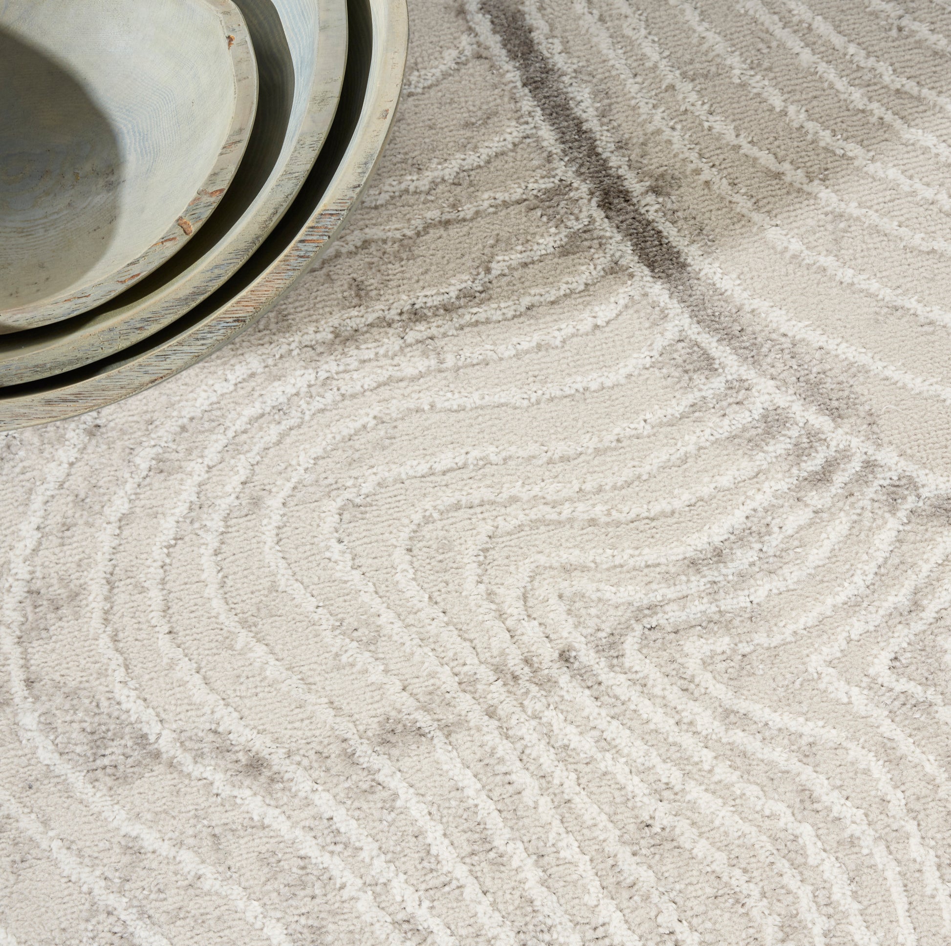 Beige tufted rug with white wavy lines; shallow ceramic bowls in pale blue-gray tones.