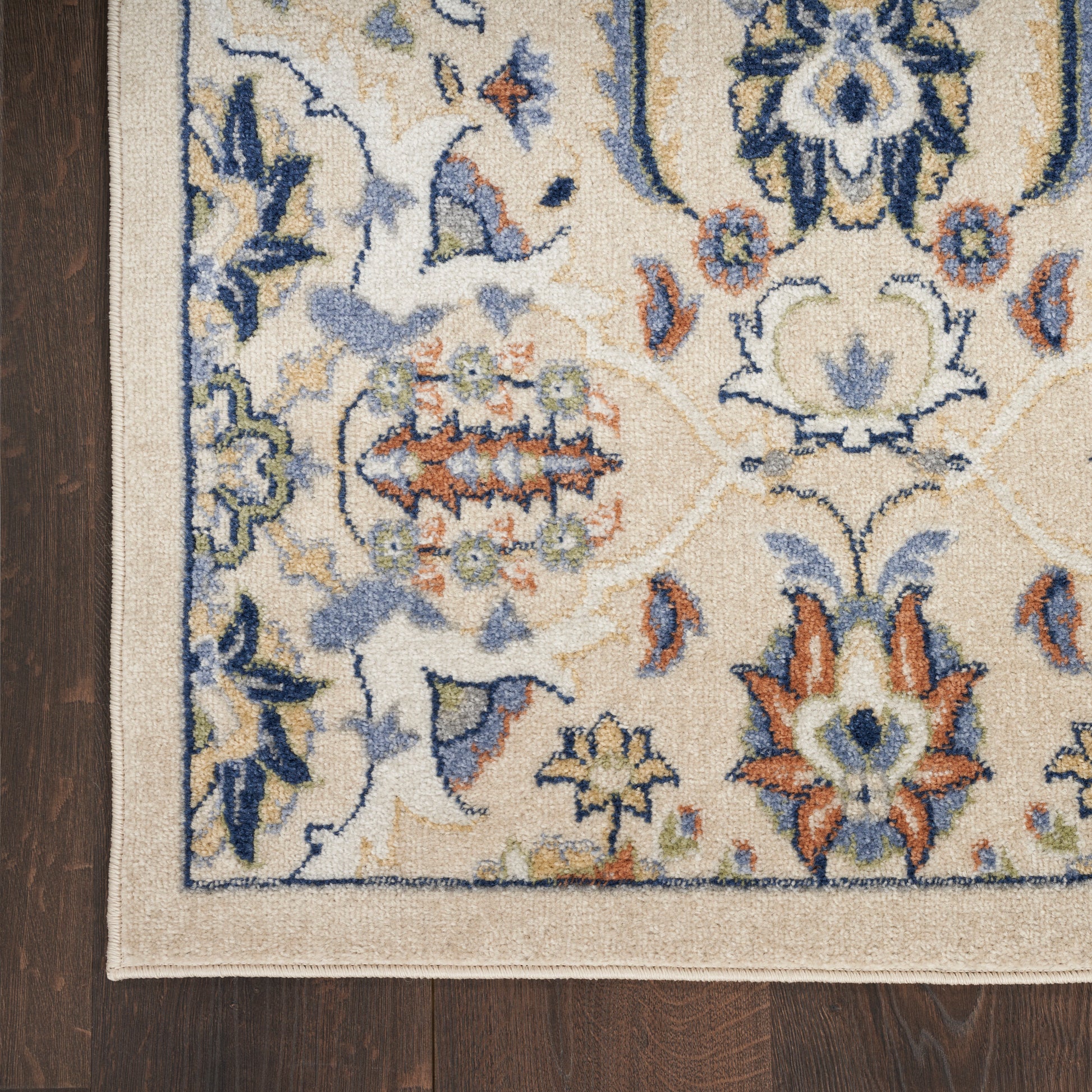 Traditional floral area rug in cream with blue, orange and green accents, bordered edge on dark wood floor.