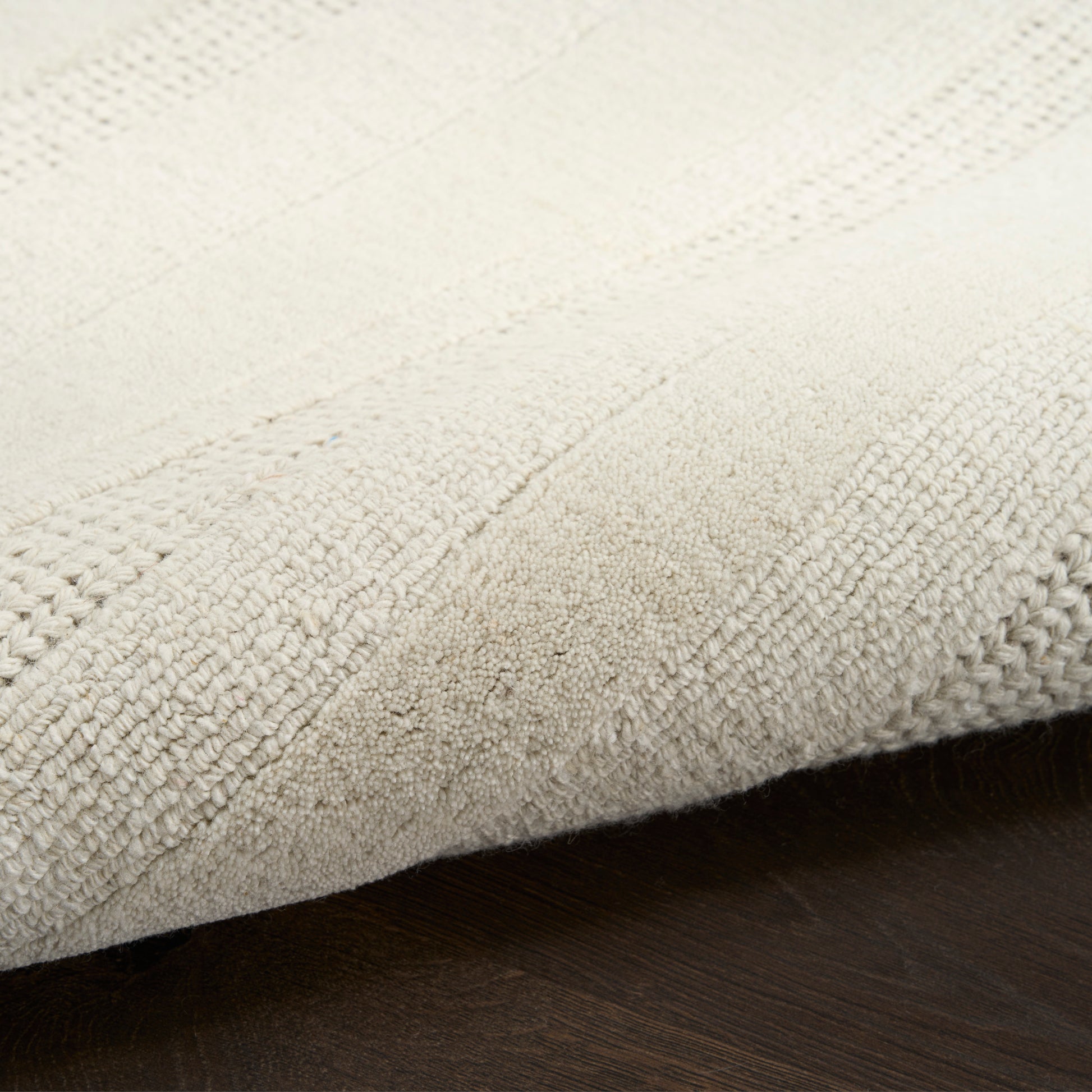 Cream textured rug with raised stripe pattern on dark wood floor.