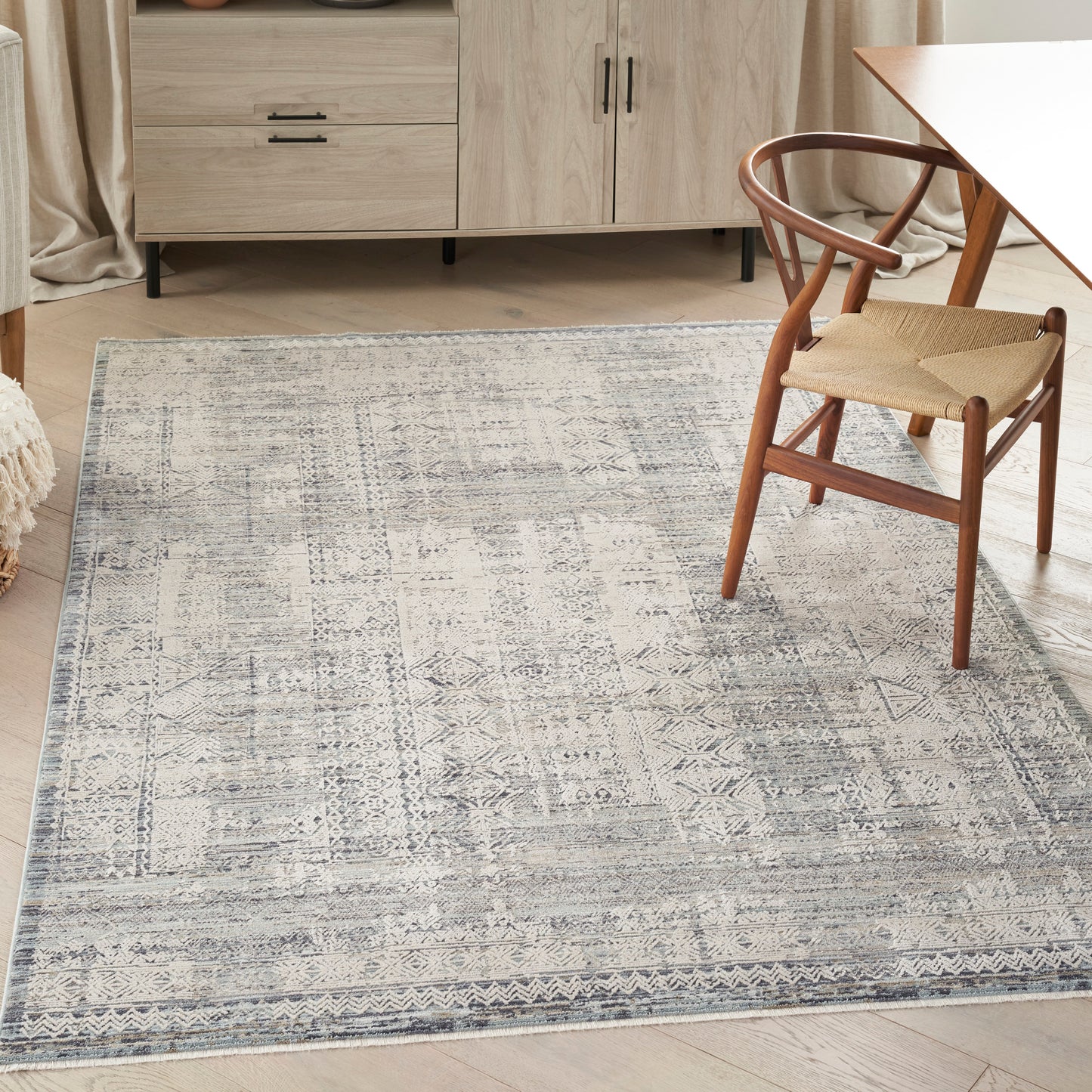 Pale blue and cream geometric patterned woven area rug on a light wood floor beside a wooden chair and dining table.