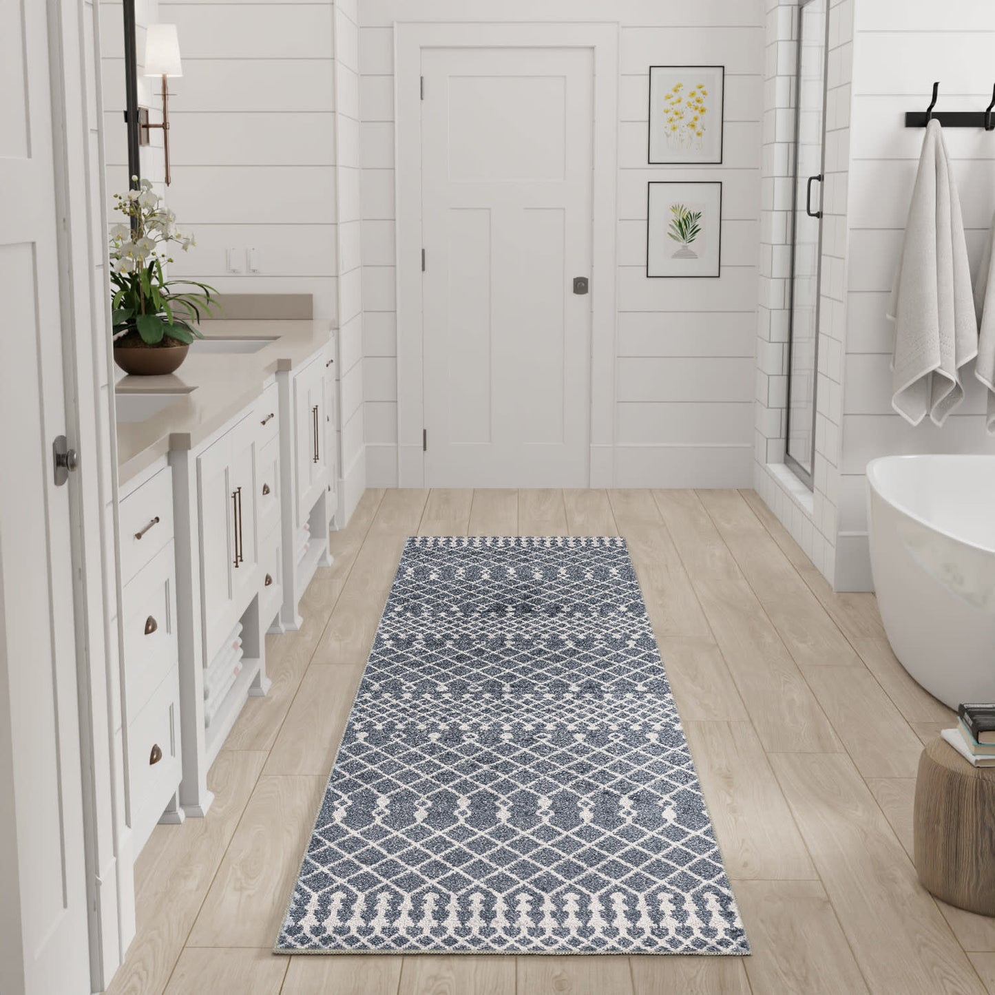 Blue and white geometric runner rug on light wood floor in a white farmhouse-style bathroom with a vanity and tub.
