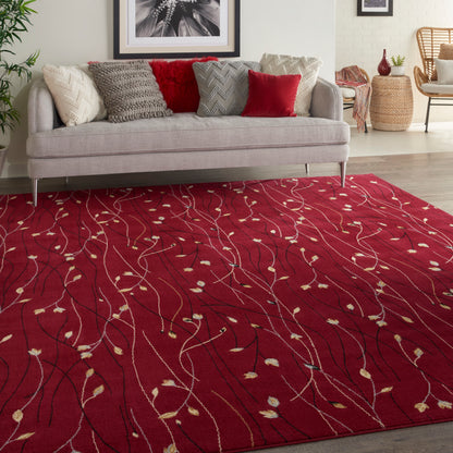 Red area rug with white vine pattern and small beige leaves under a light gray sofa with beige and red cushions.