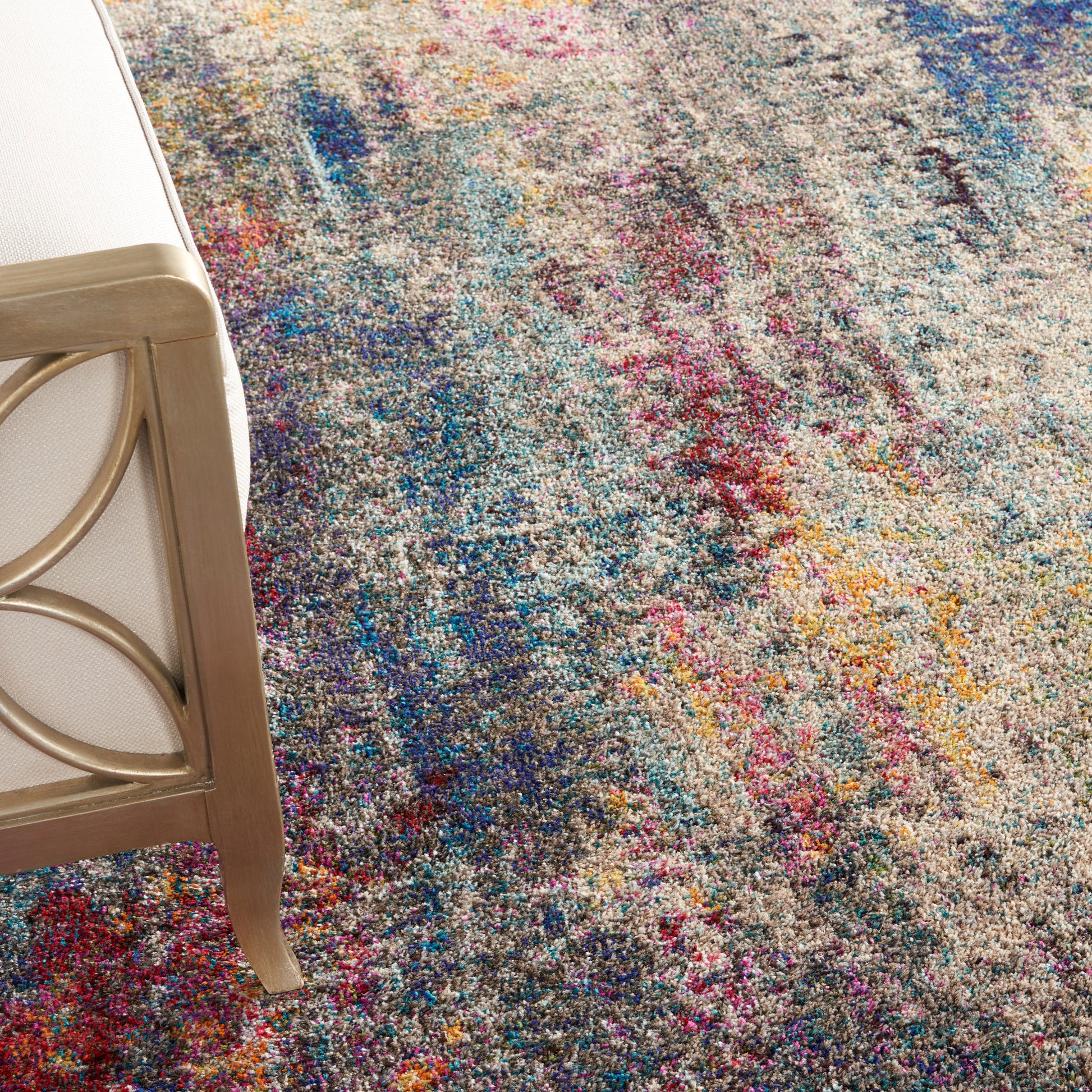 High-pile multicolor abstract area rug with blue, pink, yellow splashes; gold metal-framed chair leg visible