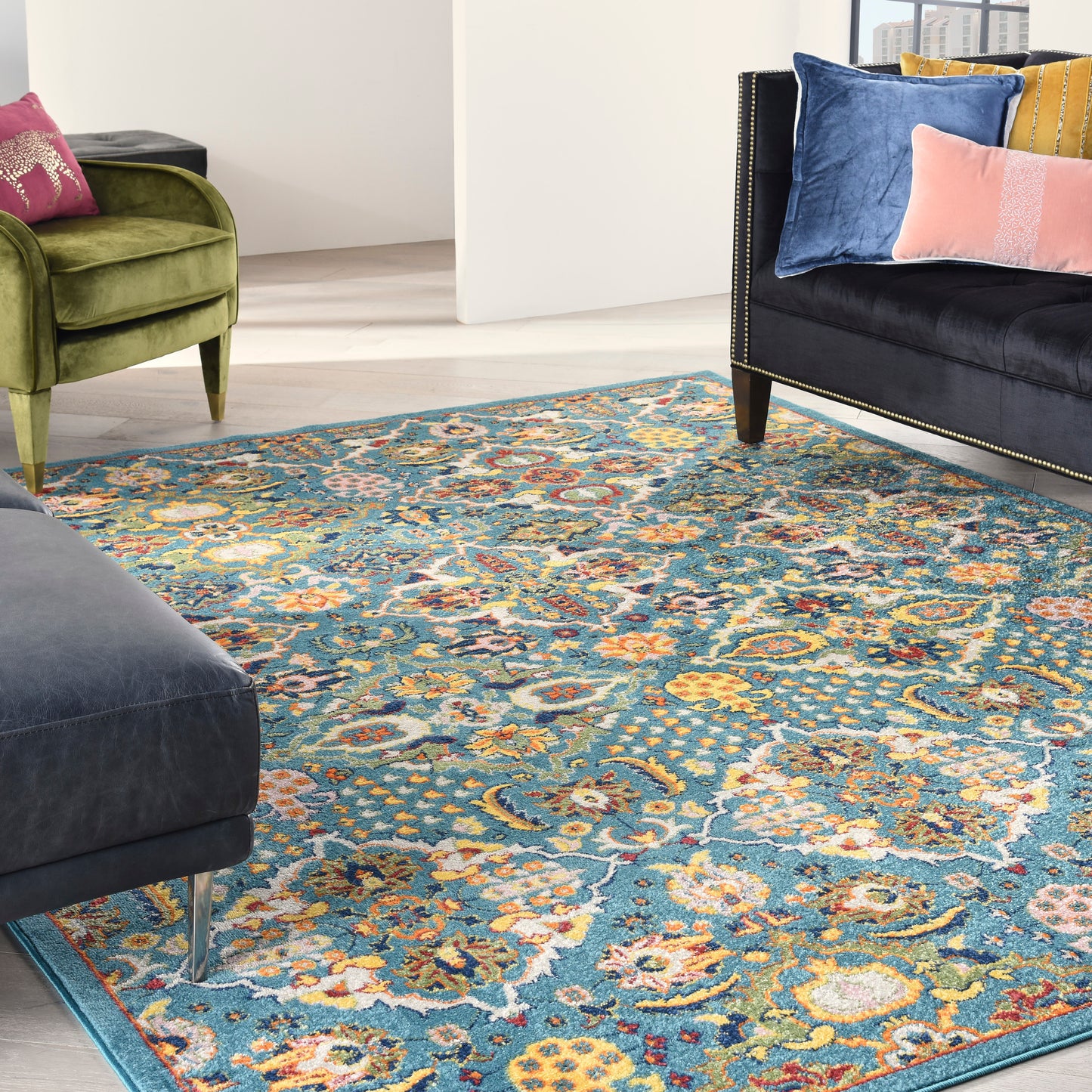 Rectangular teal rug with yellow/orange/cream motifs; green velvet armchair and navy velvet sofa with nailhead trim.