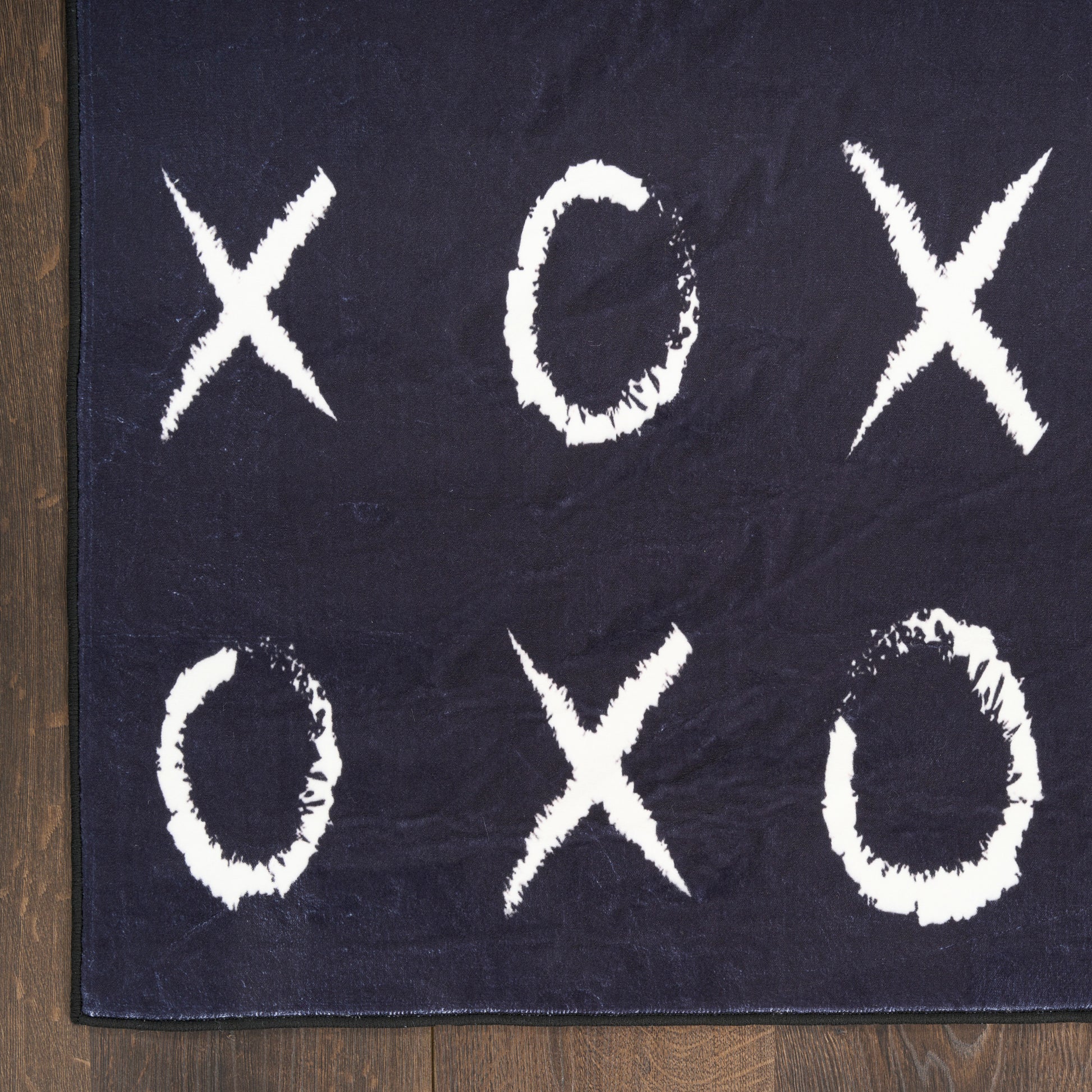 Navy tic-tac-toe rug with white chalky Xs and Os on dark fabric, placed on a wooden floor.