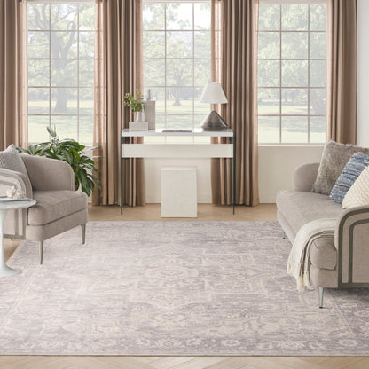 Neutral living room with beige sofas, glass console table, gray patterned rug, large windows with curtains, plants.