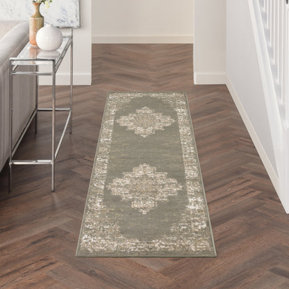 Olive-gray distressed runner rug with pale border in a hallway; dark herringbone floor and a chrome-glass console table nearby.