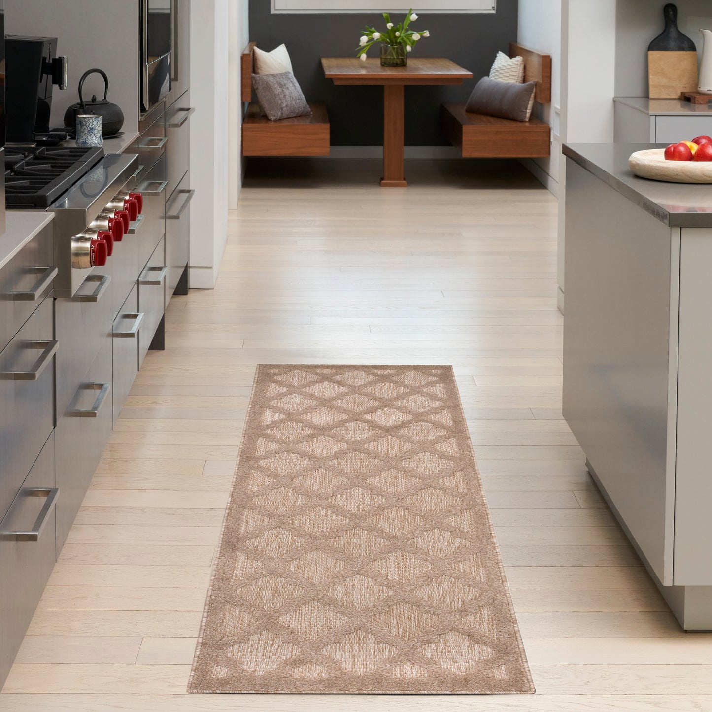 Beige geometric rug runner on light wood floor in a modern kitchen with stainless stove, island, and cozy seating at end.