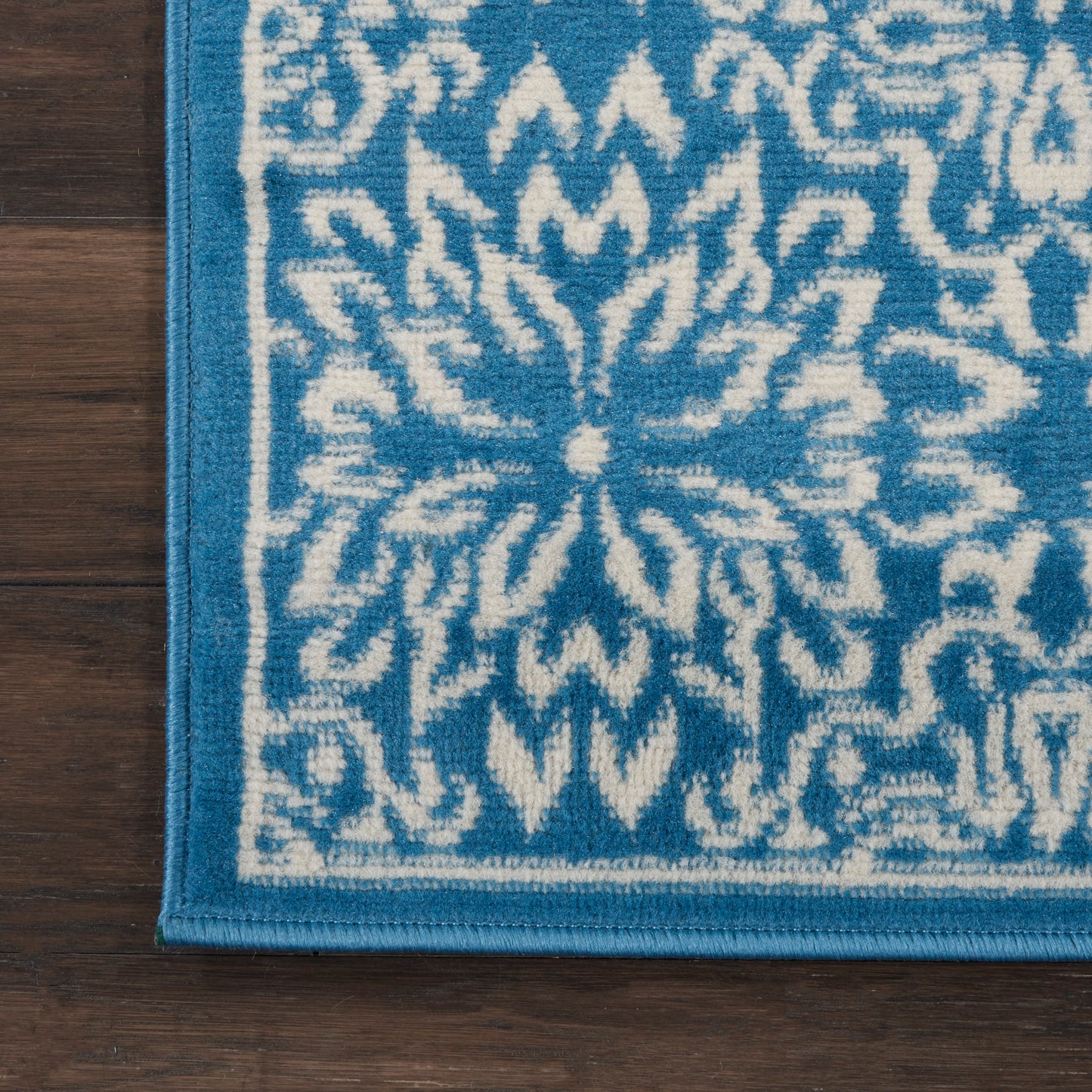 Blue and white patterned area rug with a floral medallion motif and border, close-up corner on wood floor.